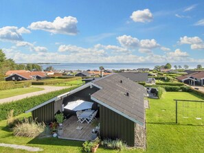 A residential area with houses, a covered outdoor seating area with a table and chairs, and a view of the sea. - 4 Star Holiday Home in Sjolund (Sjølund)