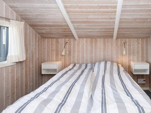 A bedroom with a wooden slat ceiling, a striped bedspread, two bedside tables, and a window with curtains. - 4 Star Holiday Home in Sjolund (Sjølund)