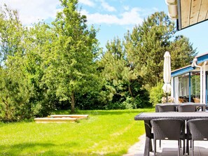 An outdoor patio area with a table and chairs, surrounded by lush greenery and trees.