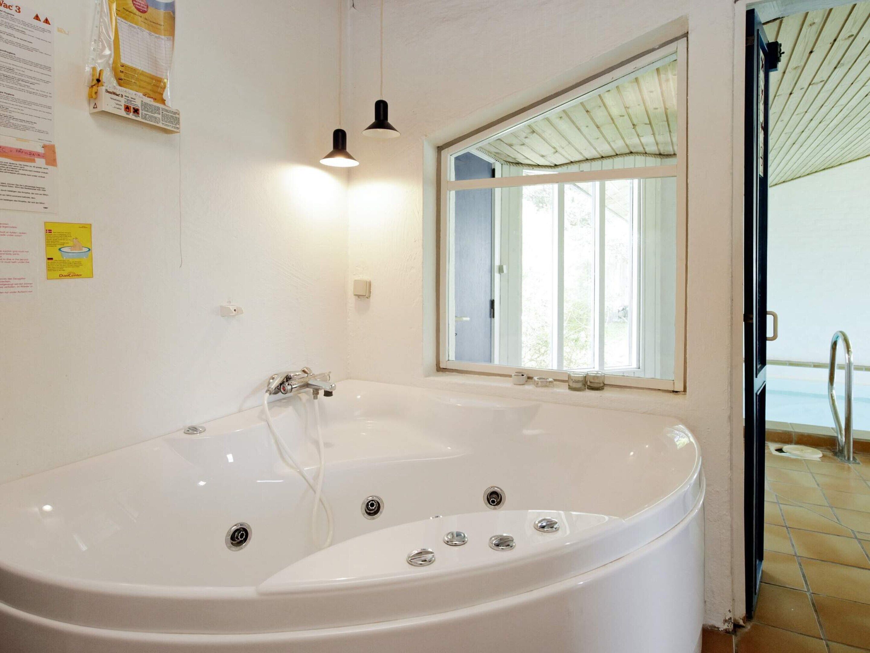 Et badeværelse med et stort badekar, et vindue og en dør, der fører til et poolområde.