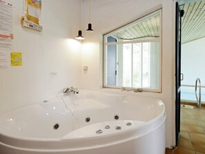 A bathroom with a large bathtub, a window, and a door leading to a pool area.
