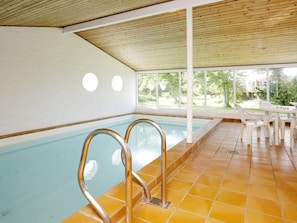 An indoor swimming pool with clear glass walls, a tiled floor, and a covered seating area with tables and chairs. - 4 Star Holiday Home in Fjerritslev (Fjerritslev)
