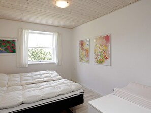 A bedroom with a bed, a window with curtains, and two wall-mounted paintings.