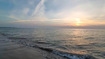 Ein Strand mit sanft anschwellenden Wellen und einem Sonnenuntergang im Hintergrund.