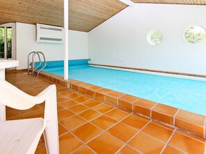 En indendørs swimmingpool med flisegulv og hvid væg.