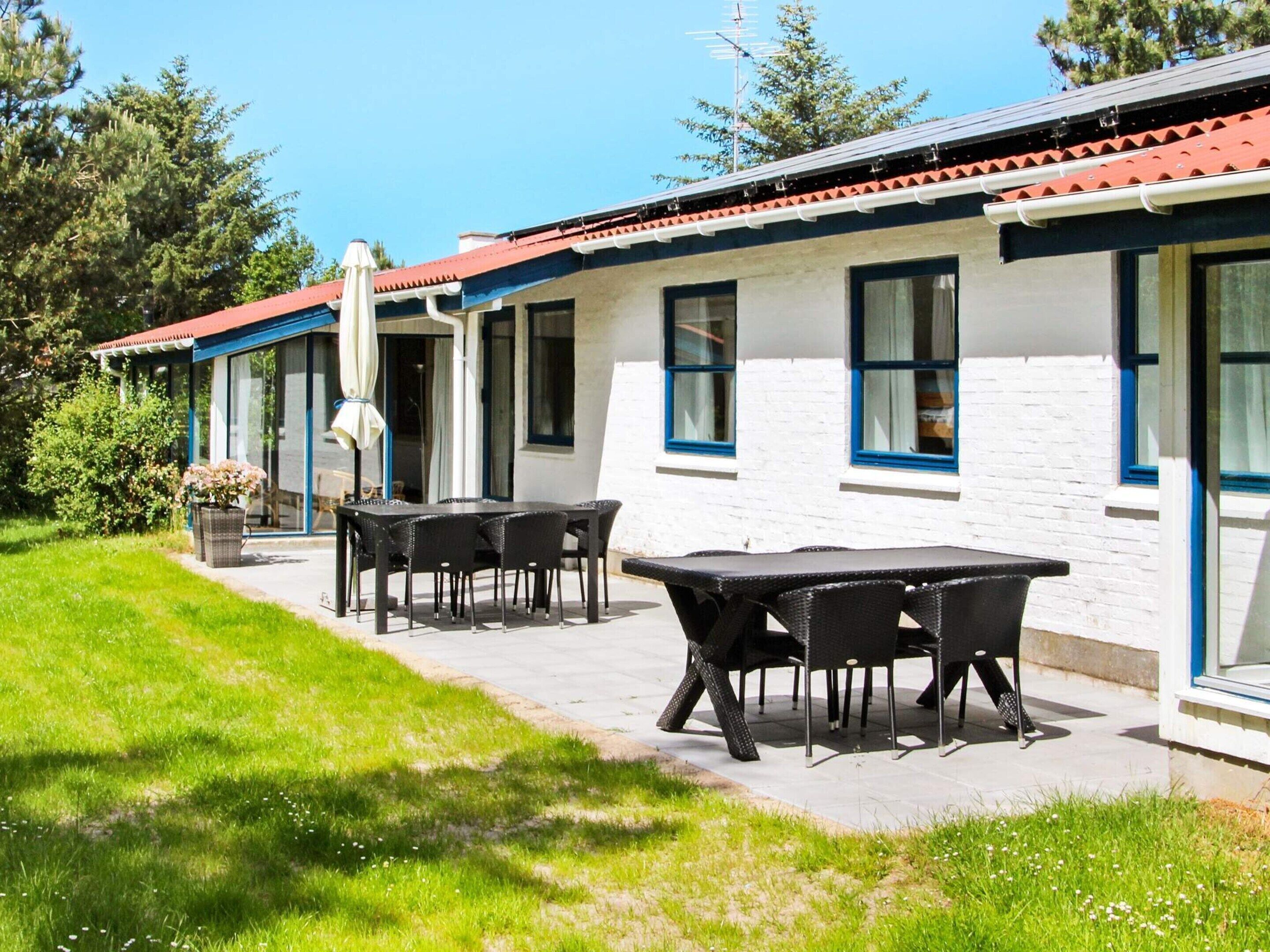 En bygning med rødt tag, hvide ydervægge og mange vinduer. Der er en terrasse med udendørs møbler.