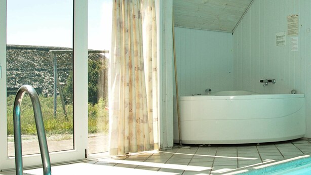 A swimming pool with a metal ladder, a hot tub, and a view of greenery outside. - Sprawling Holiday Home With Swimming Pool in Ringkøbing (Ringkobing)