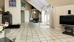 A spacious living area with a fireplace, a TV, and a dining area with chairs and a table. - Sprawling Holiday Home With Swimming Pool in Ringkøbing (Ringkobing)