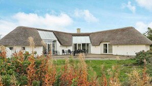 A modern house with a thatched roof, a large glass door, and a patio area with outdoor seating. - Sprawling Holiday Home With Swimming Pool in Ringkøbing (Ringkobing)