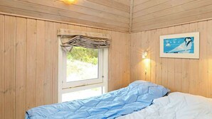 A room with wooden walls, a bed with blue bedding, a window with curtains, and a wall-mounted light fixture. - Sprawling Holiday Home With Swimming Pool in Ringkøbing (Ringkobing)