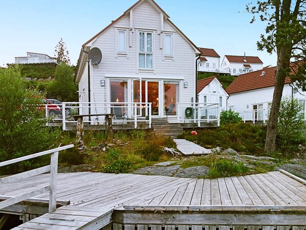 A white house with a dock and a small boat, surrounded by greenery and other houses. - Holiday Home in GurskÃ¸y (Heroy)