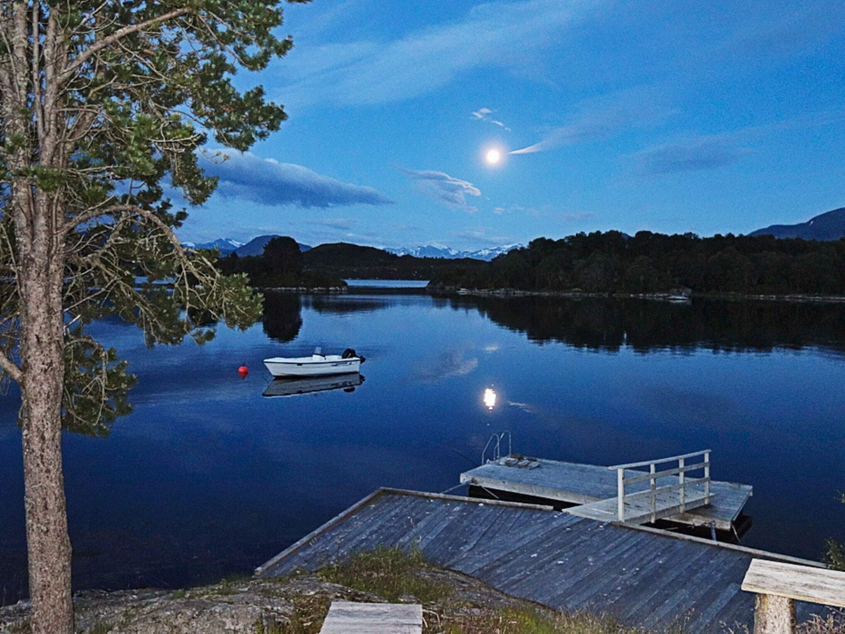 A calm lake at dusk with a dock and a boat.
