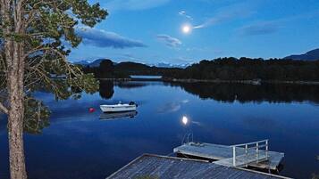 A calm lake at dusk with a dock and a boat.