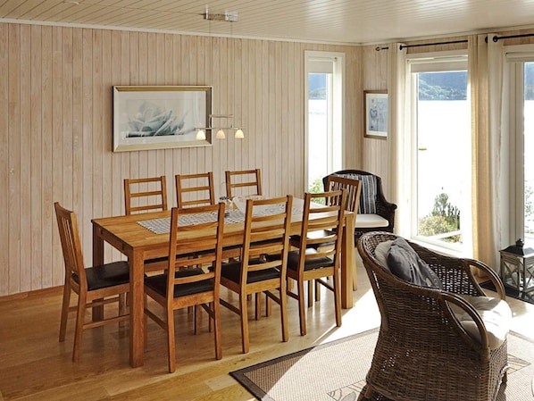 Un espace repas avec une table et des chaises en bois, un fauteuil en osier et une vue sur l’extérieur.