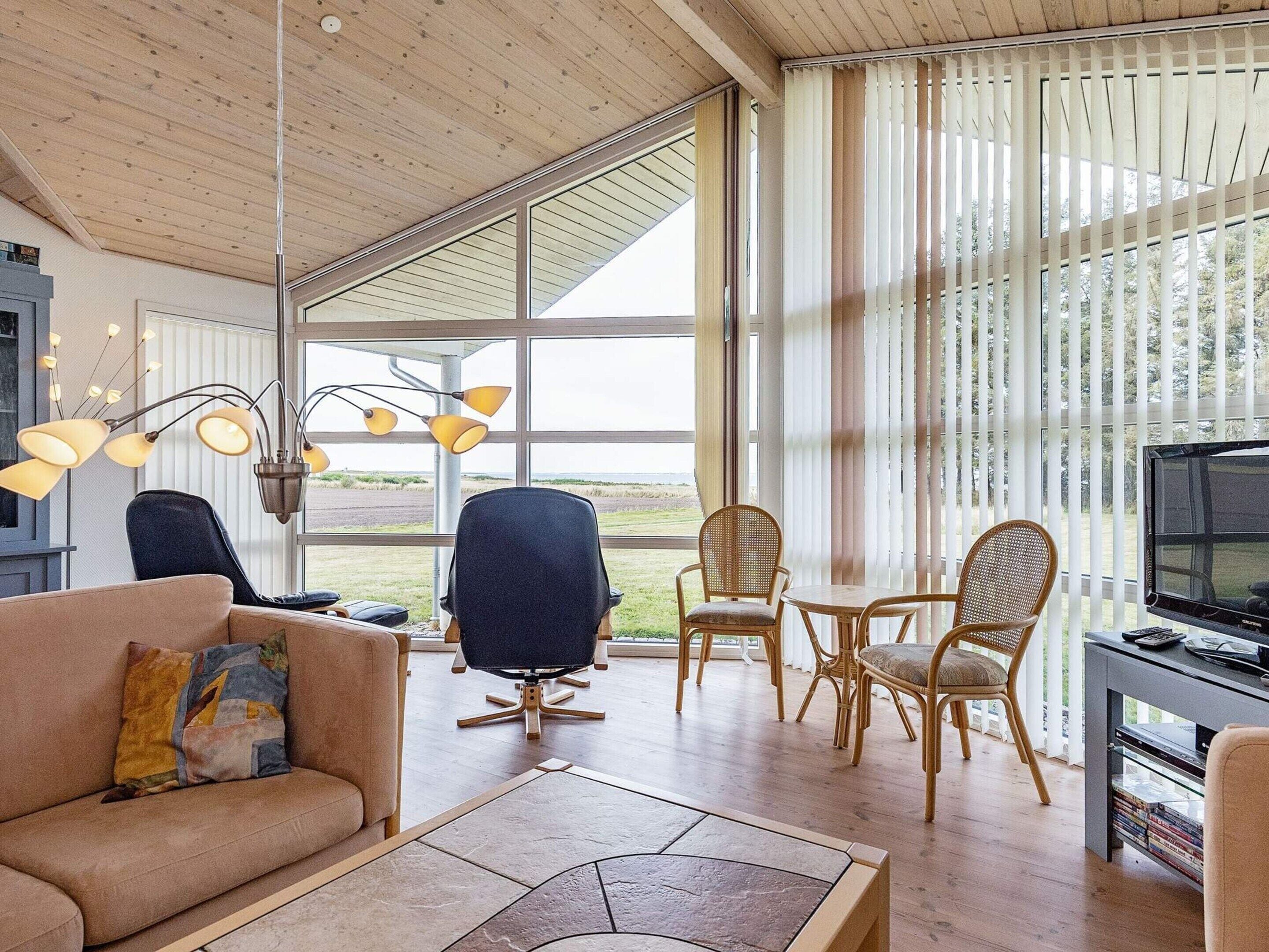 A modern living room with a large window, a sofa, a dining table with chairs, and a television.