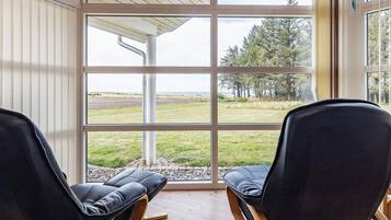 Twee zwarte stoelen met houten frame en een bekleed zitvlak, gericht op een groot raam met uitzicht op een grasveld en bomen.