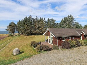 A single-story wooden house with a sloped roof, a covered porch, and a view of the sea. - 5 Star Holiday Home in Spottrup (Spøttrup)