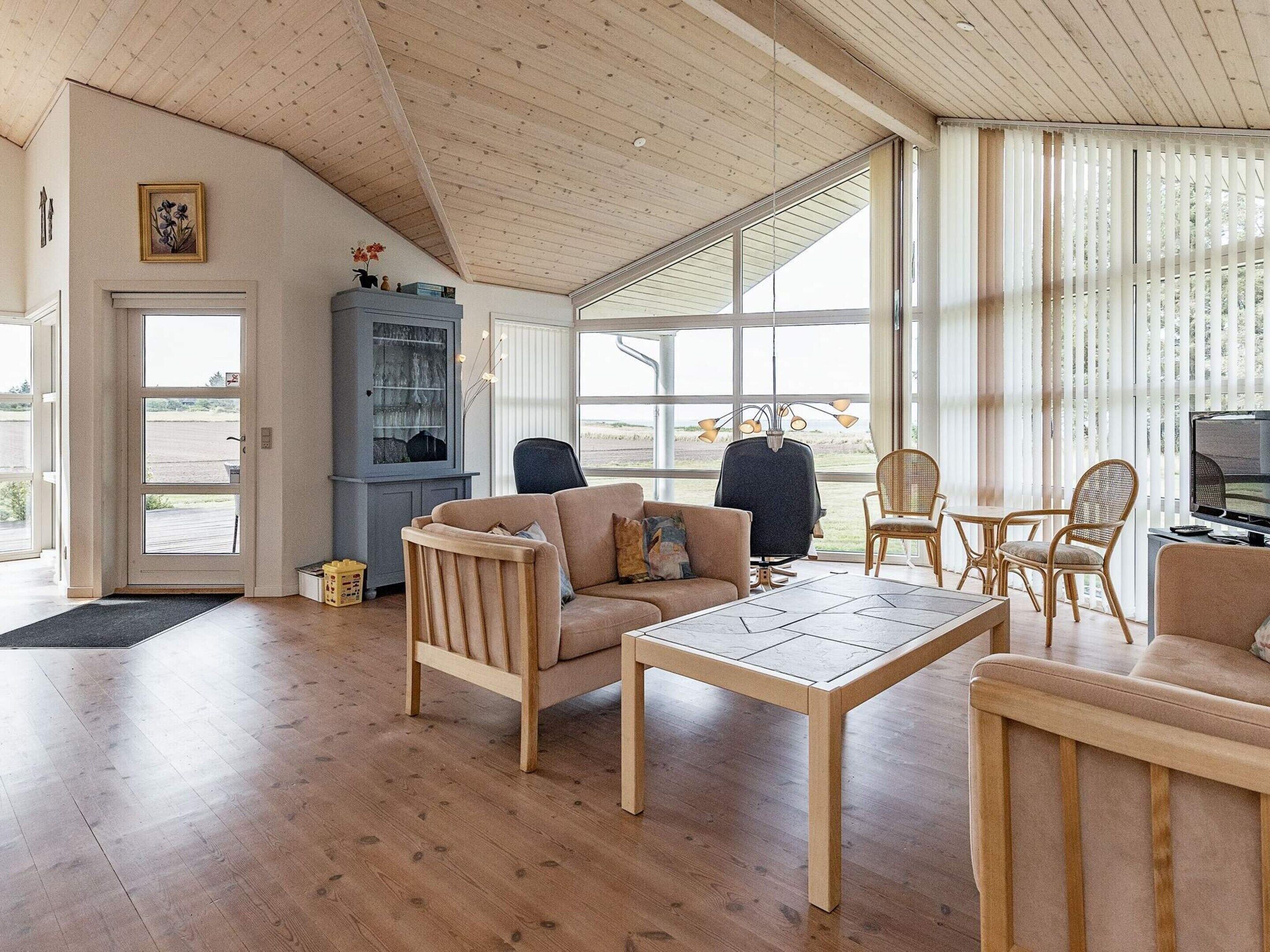 A spacious living room with wooden flooring, a high ceiling, and large windows offering a view of the outdoors.
