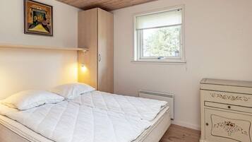 A bedroom with a bed, a nightstand, a dresser, a window, and a wall-mounted lamp.