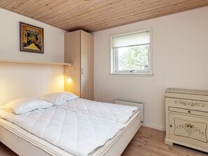A bedroom with a bed, a nightstand, a dresser, a window, and a wall-mounted lamp. - 5 Star Holiday Home in Spottrup (Spøttrup)