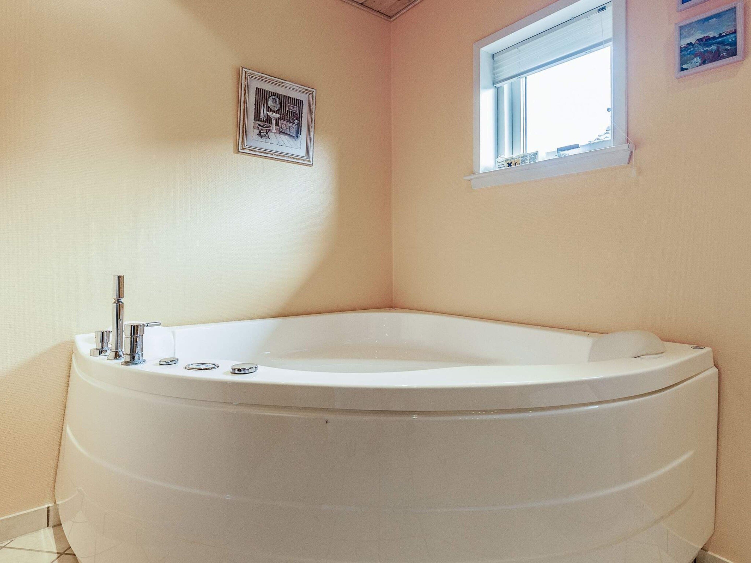 Une salle de bain d’angle avec une baignoire sur pieds, une petite fenêtre et un tableau encadré au mur.