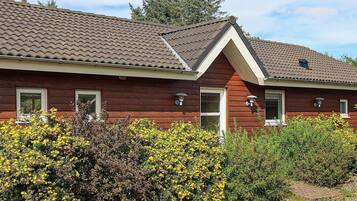 A red wooden house with a tiled roof, a front door, and two windows.