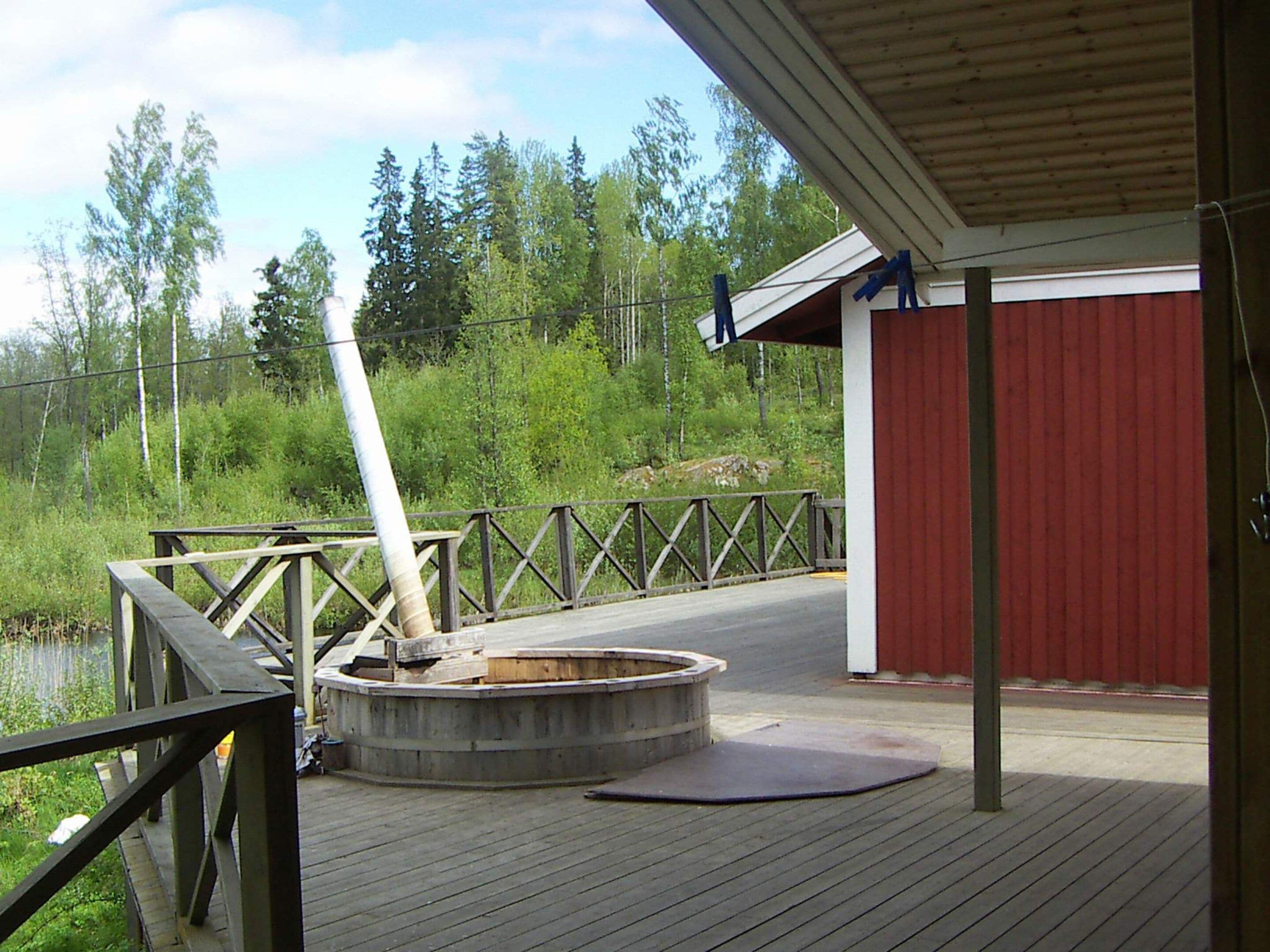 Una terraza de madera con una sauna, un edificio rojo y un paisaje natural al fondo.