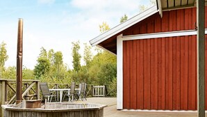 A wooden deck with a hot tub, outdoor seating, and a red building in the background. - Holiday Home in GrÃ¤smark (Gränna)