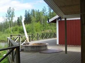 Una terraza de madera con sauna, un edificio rojo y una valla metálica.