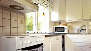 Een keuken met witte kasten, een magnetron, een koffiezetapparaat en een raam met uitzicht op groen.