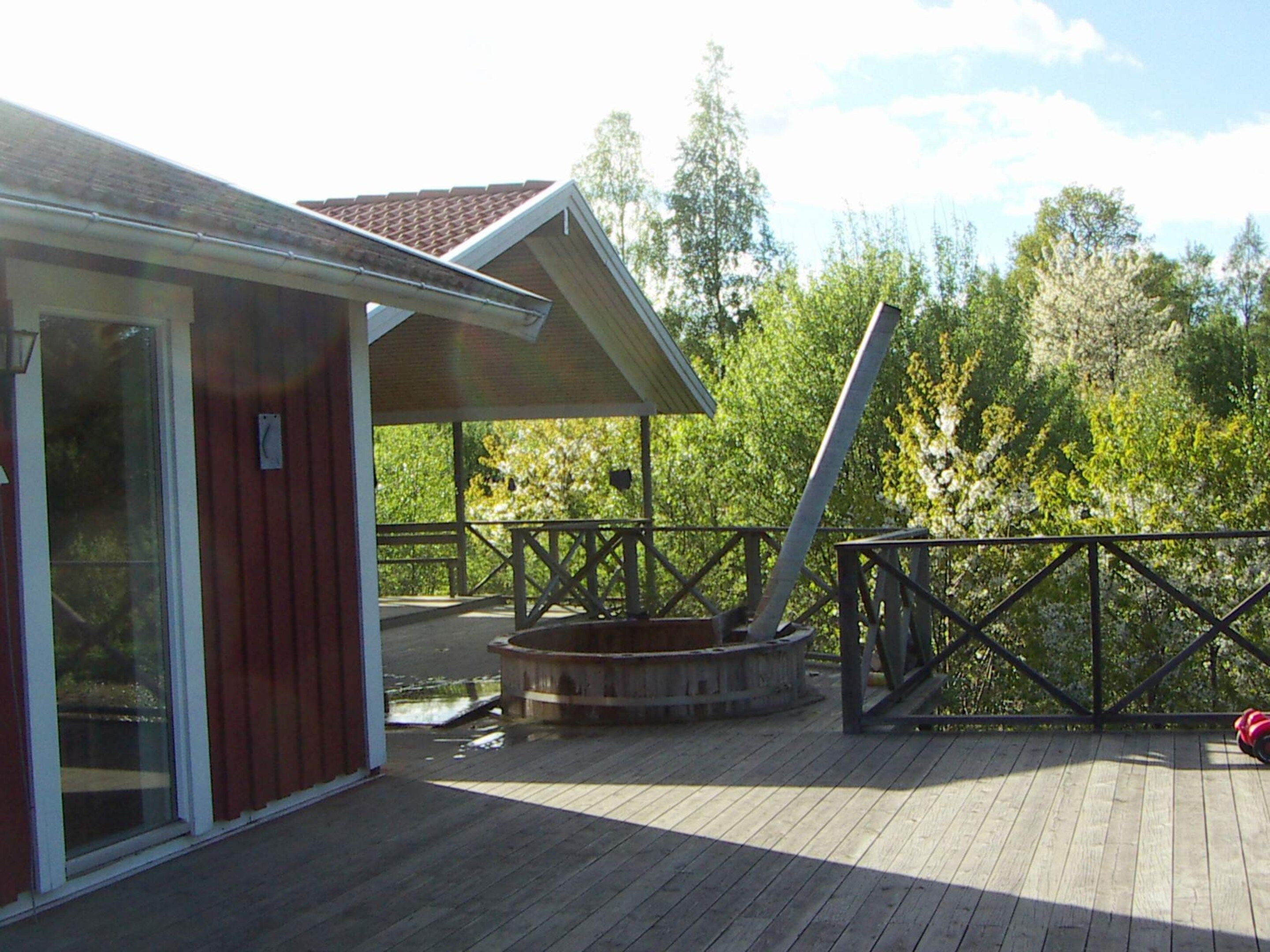 Una terraza de madera con un jacuzzi, un área techada y vistas a árboles.