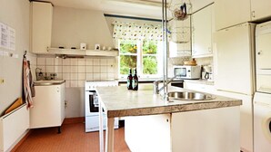 Een keuken met witte kasten, een magnetron, een spoelbak en een raam met gordijnen.