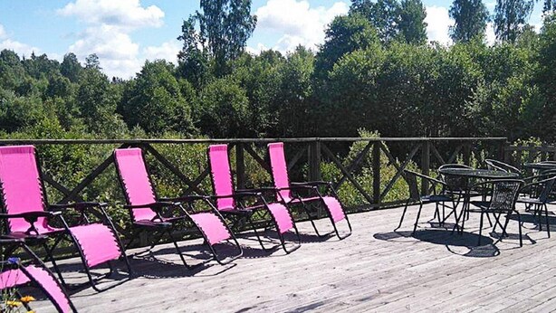Een houten terras met roze stoelen en tafels, omringd door een metalen hek.