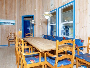 A dining area with a wooden table and chairs, a bench with floral upholstery, and a large window with blue trim.