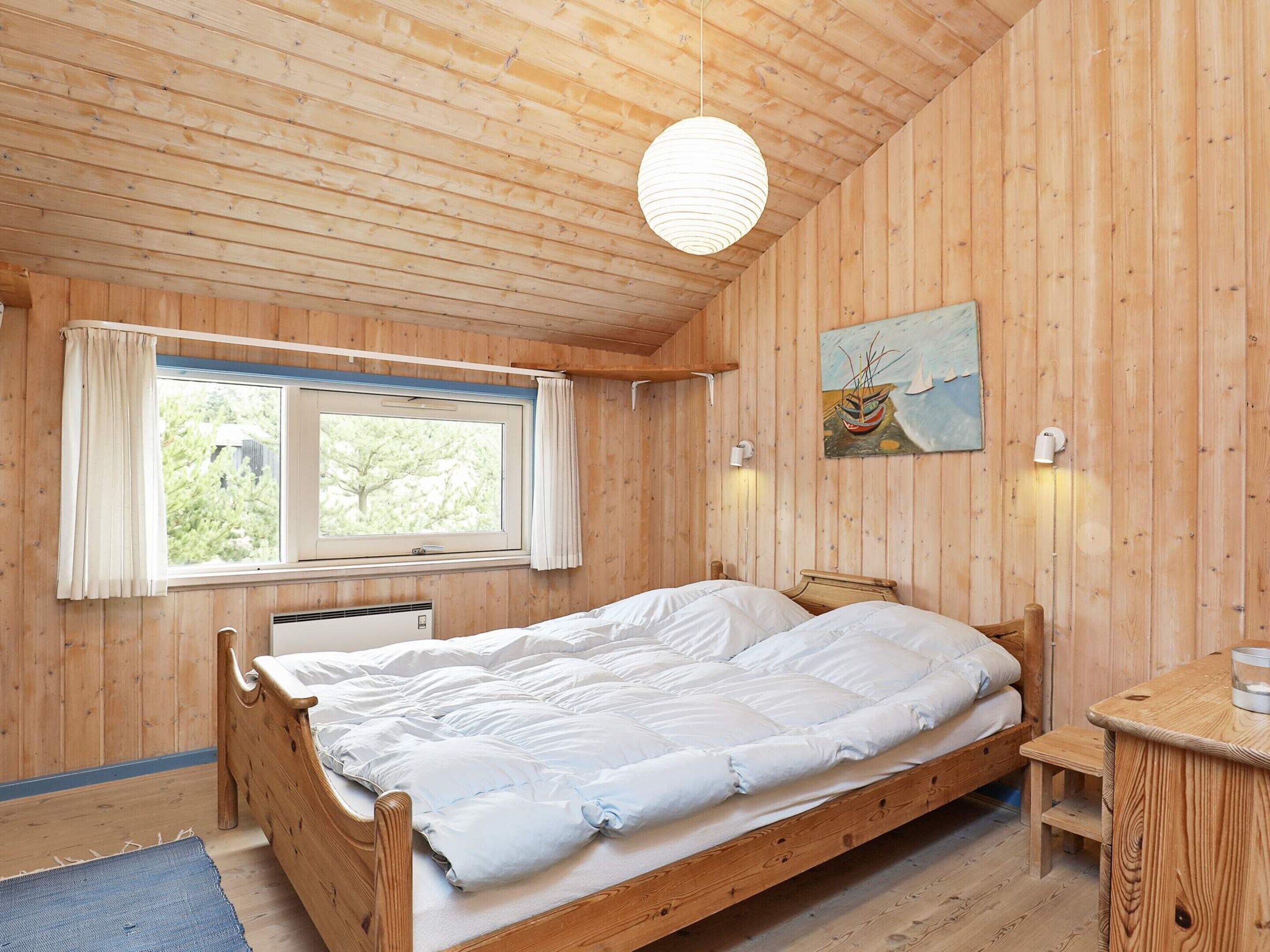 A wooden-paneled room with a bed, a window, a painting, and a bedside table.