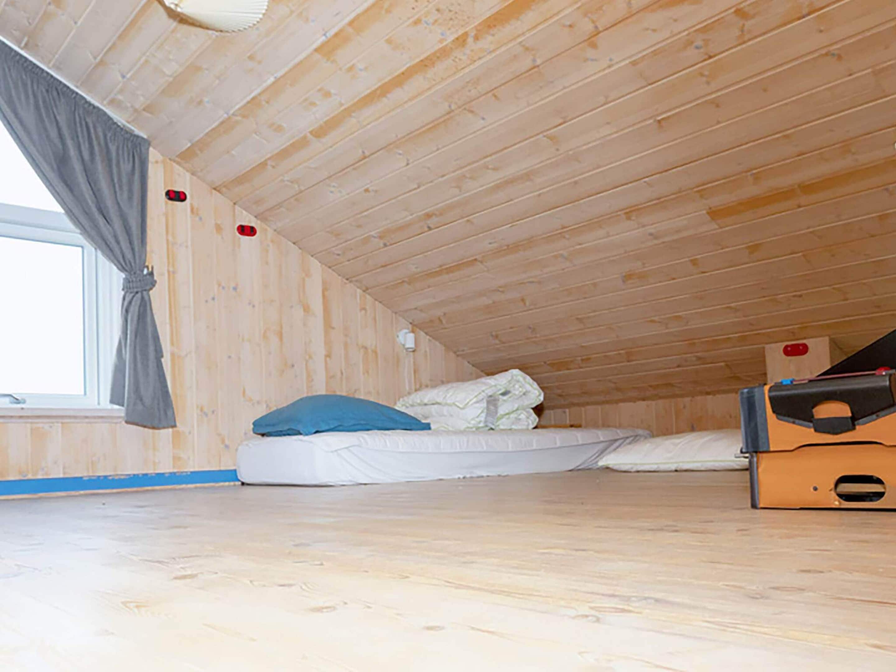 Una habitación pequeña con cama individual, techo inclinado y paredes de madera.