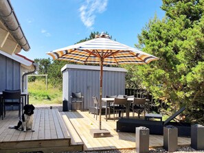 A wooden deck with outdoor furniture, a dog, and a large striped umbrella.