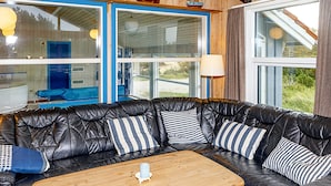 A black leather sofa with striped pillows, a wooden coffee table, and a window with curtains. - 4 Star Holiday Home in Thisted (Thisted)