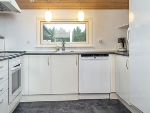 A modern kitchen with white cabinets, a dishwasher, a stove, and a window above the sink. - 4 Star Holiday Home in Romo (Rømø)
