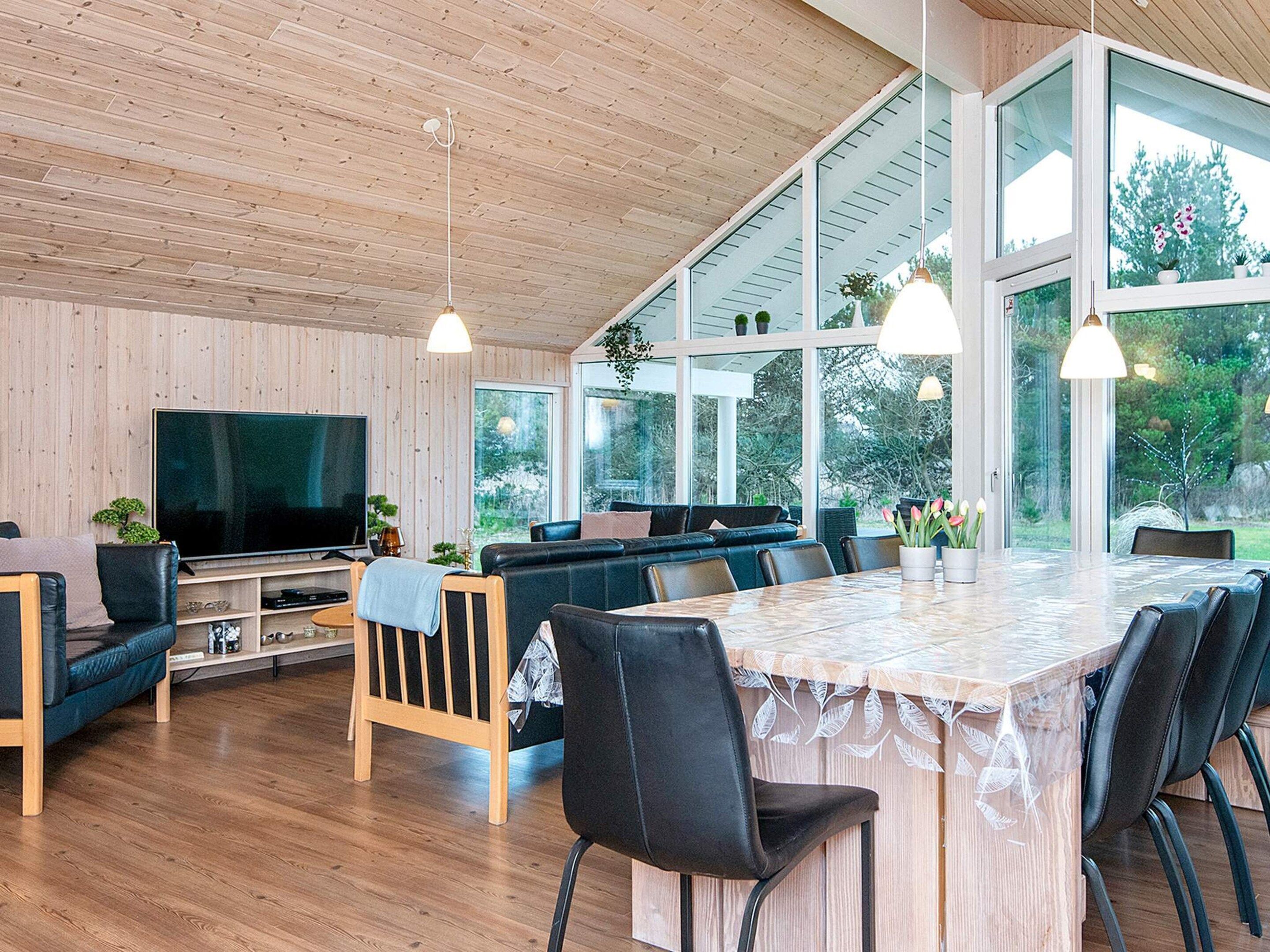 Un salon moderne doté d’un grand téléviseur, de murs recouverts de panneaux en bois, d’un canapé et d’un coin repas avec une table et des chaises.