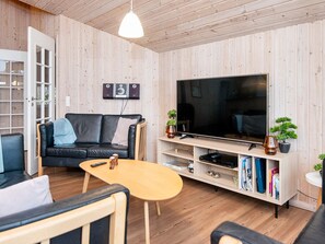A modern living room with a black leather sofa, a wooden coffee table, a flat-screen TV, and a bookshelf. - 4 Star Holiday Home in Romo (Rømø)
