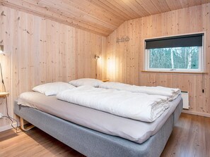 A room with a bed, wooden walls, a window, and a lamp.