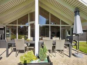 En utomhusveranda med tak, möbler av rotting, en liten trädgård och en pergola.