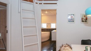 Una habitación con una puerta blanca que da al baño, una escalera blanca y un comedor con mesa y sillas.