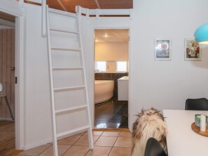 Una habitación con una puerta blanca que da al baño, una escalera blanca y un comedor con mesa y sillas.