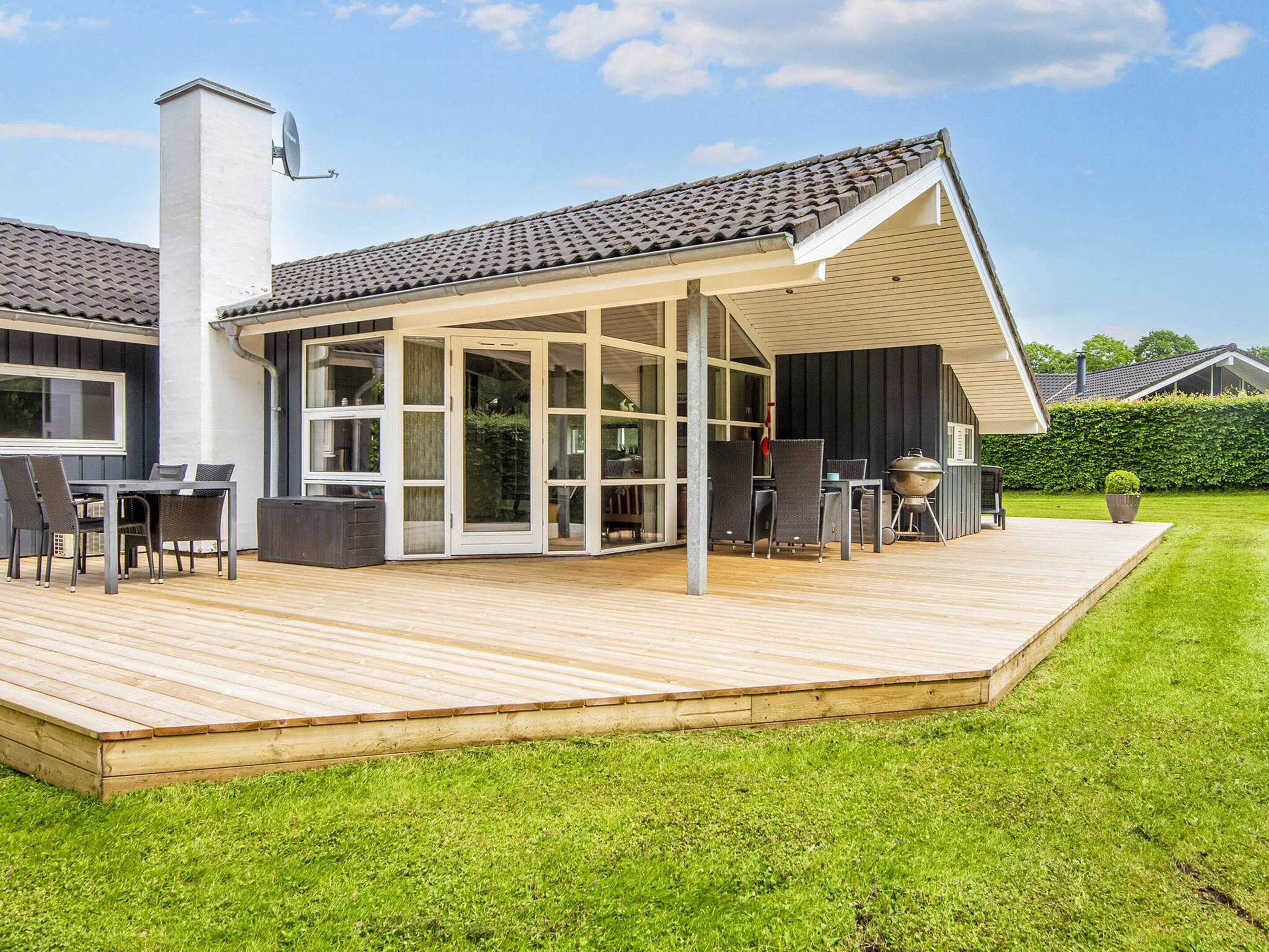 A modern house with a covered patio, a barbecue, and a dining area with outdoor furniture.