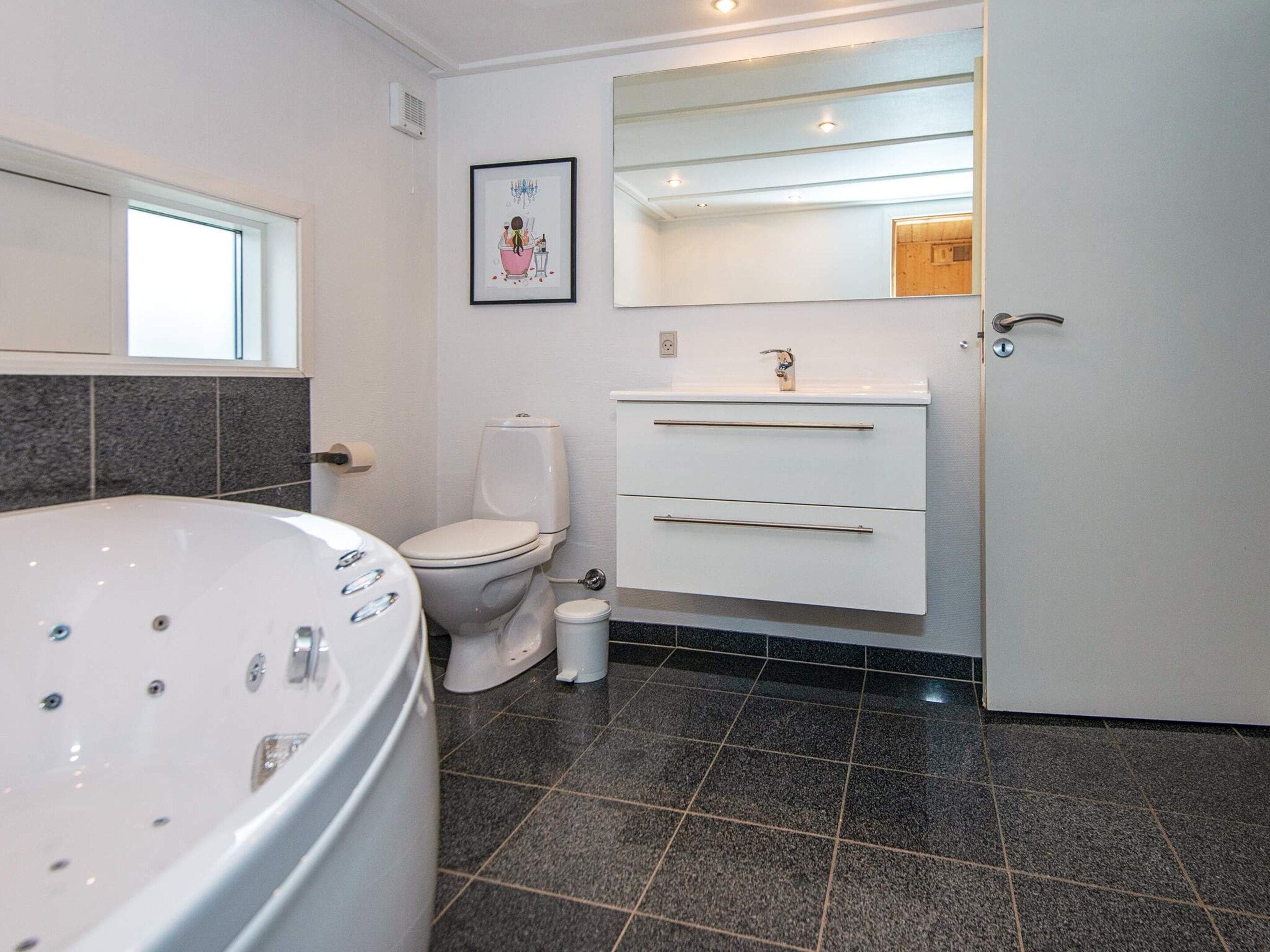 A modern bathroom with a bathtub, toilet, vanity with drawers, and a mirror.