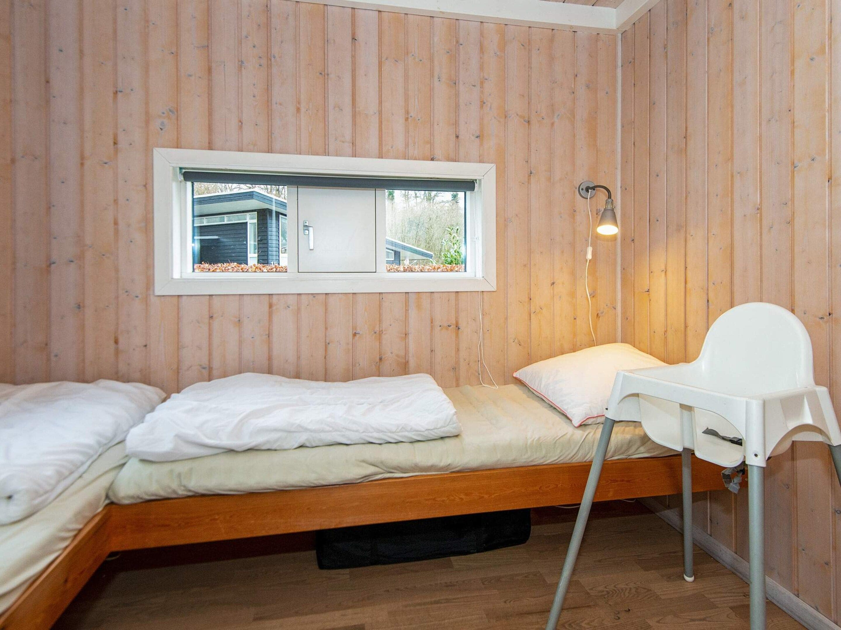 Une petite chambre avec un lit simple, des murs en bois, une fenêtre, une table de chevet et une chaise.