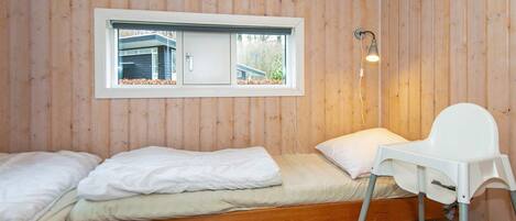 Une petite chambre avec un lit simple, des murs en bois, une fenêtre, une table de chevet et une chaise.