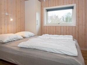 Une chambre à coucher avec un lit, des oreillers, une fenêtre et des murs en bois.